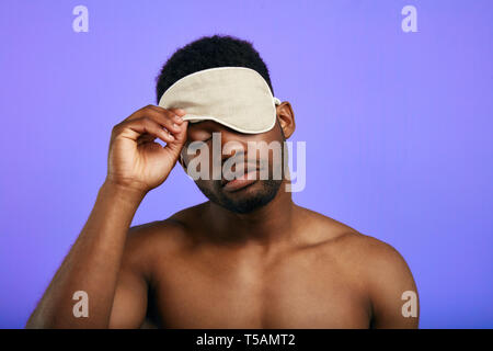 Schläfrig, müde Mann weg nehmen oder das Setzen auf die schlafbrille. nach oben Porträt schließen. Isolierte blauen Hintergrund. Müdigkeit Konzept. Stockfoto