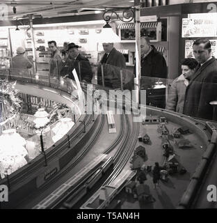 1950, historische, Personen, die in einem großen Zug set, Tri-ang Eisenbahn, in der Mitte des Hamleys Toy Shop, London, England angezeigt. Stockfoto