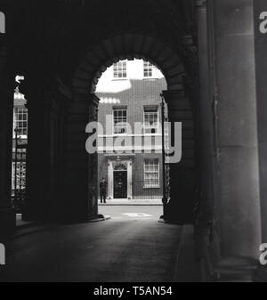 1960 s, historischen, einen Blick durch einen Torbogen von Downing Street Nr.10, London, der Heimat der Premierminister von Großbritannien, mit einem britischen Polizist Stand anwesend. Ursprünglich 3 Georgianische Häuser, sie wurden zu den Ersten Lord der Schatzkammer von König Georg II. und zu einem Haus von William Kent für Sir Robert Walpole. Stockfoto