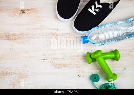 Turnschuhe, Kurzhanteln, eine Flasche Wasser und ein Maßband auf einer hölzernen Hintergrund. Konzept für einen gesunden Lebensstil und Sport. Stockfoto