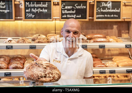 17. April 2019, Hessen, Steinau an der Straße: Bäckermeister Jürgen Fink steht in seinem verkaufsraum und übergibt ein Roggenbrot, deren Maserung von einem lokalen Landwirt angebaut wird. Unter dem Motto "Backen mit Liebe und Zeit', die Firma, die Familie seit vielen Generationen im Familienbesitz, arbeitet nach alten handwerklichen Traditionen ohne industrielle Backmischungen oder tiefgekühlte Teige. Foto: Frank Rumpenhorst/dpa Stockfoto