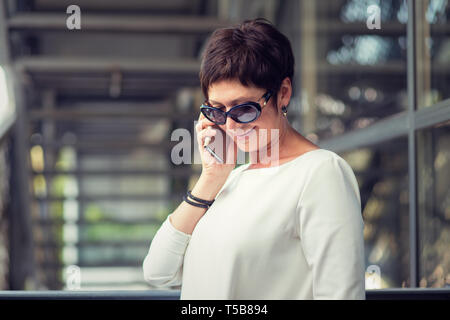 Am Telefon sprechen lächelnd. Seite Profil ansehen Portrait von Happy reife Lady mit Smart Phone, städtischen Metalltreppe auf Hintergrund. Modell Stockfoto