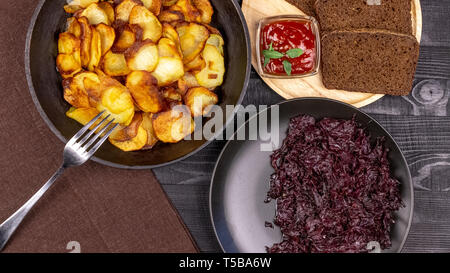 Fried Potato Chips in einem Topf mit dunkle Roggenbrot auf einer Holzplatte und hausgemachte gedünstetem Kohl, auf einem schwarzen Hintergrund im Landhausstil. Ansicht von oben Stockfoto