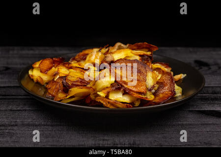 Gebratene hausgemachte Kartoffelchips in einer schwarzen Platte auf einer hölzernen rustikalen Hintergrund. Stockfoto