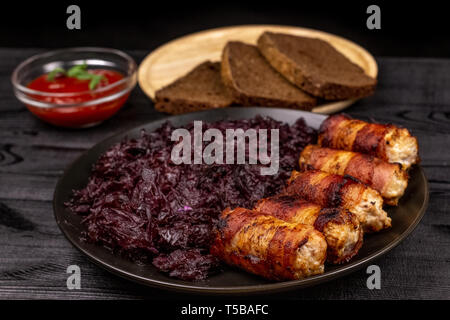 Gebratene hausgemachte gegrillte Würstchen oder chevapchichi mit Schmorkohl und Scheiben Roggenbrot und Tomatensauce auf Holz rustikale Hintergrund. Stockfoto