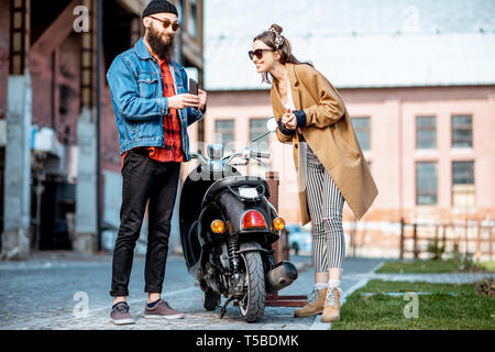 Stilvolle junger Mann und Frau zusammen gesprochen, in der Nähe der retro ständigen Moped draußen auf der industriellen städtischen Hintergrund Stockfoto
