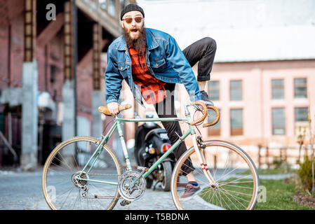 Portrait eines bärtigen Mann wie ein Verrückter hipster Spaß mit retro Fahrrad draußen auf der industriellen städtischen Hintergrund Stockfoto