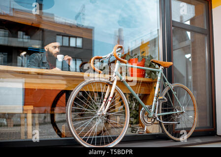 Stilvolle Mann genießen Sie Kaffee trinken, während im Cafe in der Nähe der Fenster mit retro Fahrrad sitzen. Weiten Blick durch das Fenster Stockfoto