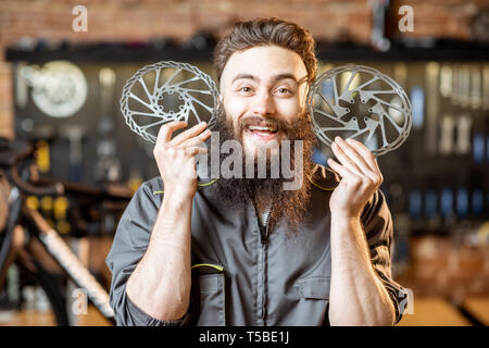 Porträt einer stattlichen bärtigen Handwerker in Arbeitskleidung mit Bremsscheiben in der fahrradwerkstatt Stockfoto