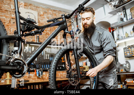 Schöne bärtige Handwerker in Arbeitskleidung Montage Rad mit dem Mountainbike in der Werkstatt Stockfoto