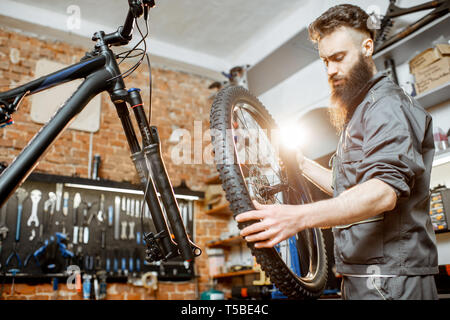 Stattliche Handwerker in Arbeitskleidung, Mountainbike, stehend mit Vorderrad in der Werkstatt eines Fahrrad Shop Stockfoto