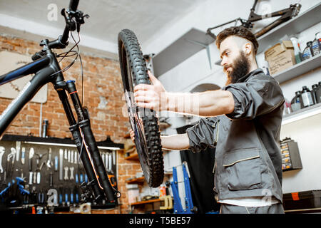 Stattliche Handwerker in Arbeitskleidung, Mountainbike, stehend mit Vorderrad in der Werkstatt eines Fahrrad Shop Stockfoto