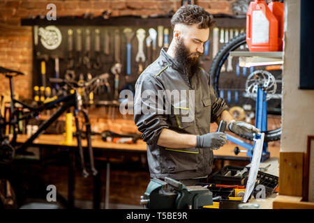 Schöne bärtige Handwerker in Arbeitskleidung, die in der wunderschönen Fahrrad Werkstatt Stockfoto