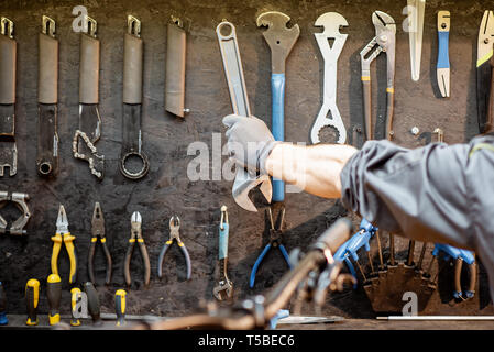 Mann, die Schlüssel von der schwarzen Wand mit verschiedenen Tools für Fahrrad reparieren Stockfoto