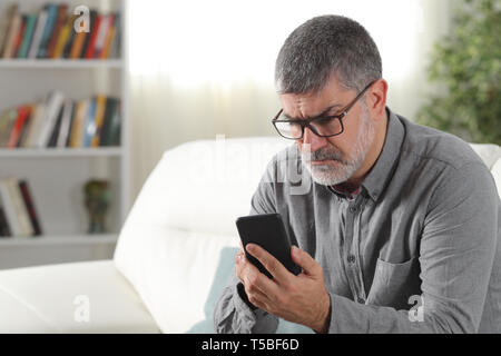 Verwirrt Mitte alter Mann mit einem Smart Phone auf der Couch zu Hause sitzen Stockfoto