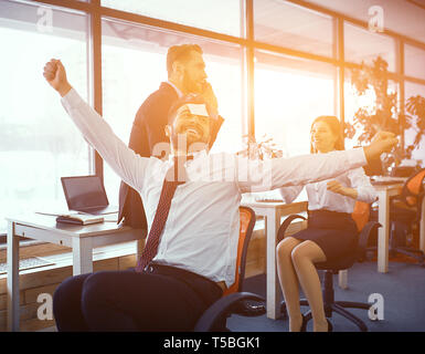 Bärtiger Mann mit Aufkleber auf seiner Stirn spielt die Narren im sonnigen Büro. Lustige Momente der Kollegen. Stockfoto