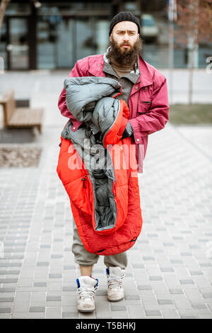 Porträt einer gedrückt und Obdachlose Bettler stehen mit Schlafsack in der Nähe der Business Center im Freien Stockfoto