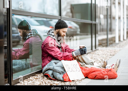 Obdachlose Bettler mit Schlafsack Betteln Geld in der Nähe der Business Center gewickelt. Konzept der Armut und Arbeitslosigkeit Stockfoto
