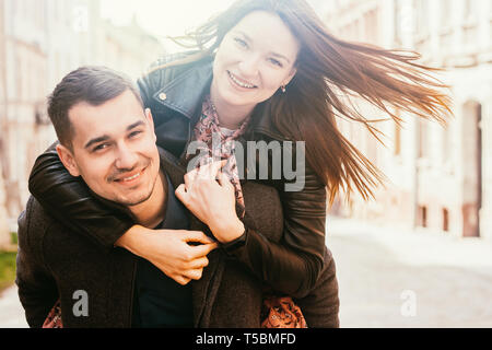 Junger Mann, der piggyback Ride zu seiner Freundin. Glückliches Paar in der Straße. Stockfoto