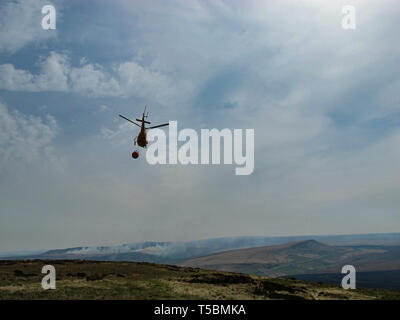 Marsden, Großbritannien. 23. April 2019. Moorland Brände in der nähe von Marsden. Ein Helikopter fliegt, Brände auf Moorland oben Marsden, West Yorkshire zu kämpfen. Stockfoto