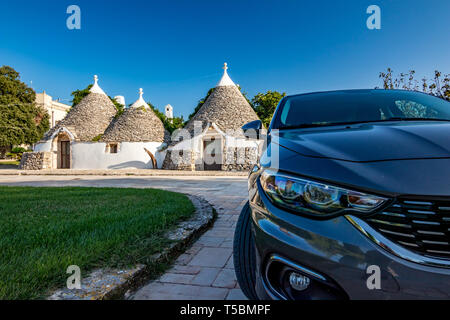 Morgen Foto von typisch italienischen Truli in der Nähe von Alberobello in der Region Apulien. Trulli sind als UNESCO-Weltkulturerbe. Defokussierten vorderen Teil der modernen Auto im Vordergrund. Klar Sommer August blauer Himmel Stockfoto