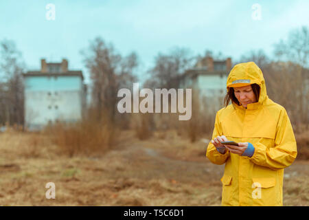 Frau im gelben Regenmantel SMS auf Handy im Freien an regnerischen Tag Stockfoto