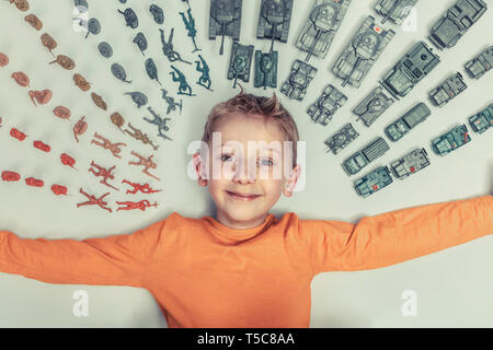 Portrait von Happy 6 Jahre alten Jungen auf dem Boden liegen und durch militärische umgeben - themed Plastikspielzeug. Stockfoto