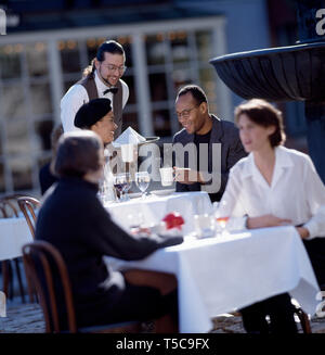 Gerne Mitte nach Paar wird von einem lächelnden Kellner an ihren Tisch in einem Restaurant serviert. Stockfoto