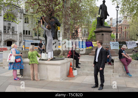 Frauen Mitkämpfer Position eine große Topfpflanzen Baum an den Füßen von Nelson Mandelas Statue im Parlament Platz während der einwöchigen Protest vom Klimawandel Aktivisten mit Kampagne der Auslöschung Rebellion Kreuzungen und Brücken rund um die Hauptstadt zu blockieren, am 23. April 2019 in London, England. Stockfoto