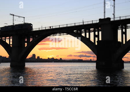 Silhouette von gewölbten Bahnbrücke und einen Zug bei Sonnenuntergang. Dnjepr, Dnipo Stadt, Dnepropetrovsk, Ukraine. Stockfoto