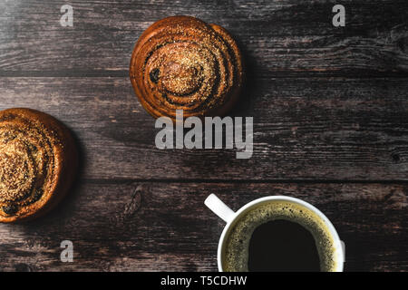 Perfektes Frühstück mit hausgemachten Zimt Brötchen und Kaffee auf Holztisch. Im rustikalen Stil. Stockfoto