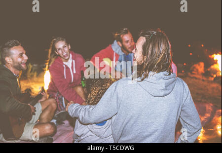 Gruppe von Freunden Spaß haben, Gitarre spielen neben dem Lagerfeuer in der Nacht - glückliche junge Leute zusammen Camping lachen und Bier trinken. Stockfoto