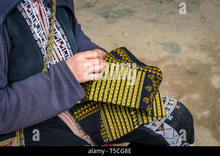 Roten Dzao ethnische Minderheit Frau nähen in Sa Pa, Lao Cai Provinz, Vietnam. Eine ältere Frau näht auf der Straße. Schöne Stickerei als souveni Stockfoto