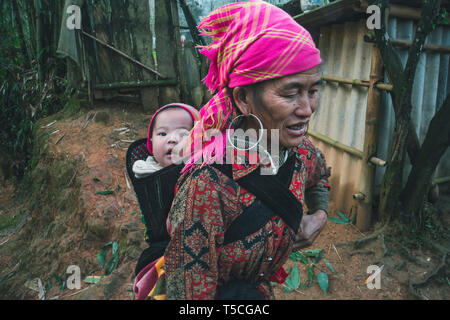 TA PHIN, Lao Cai, VIETNAM - 12. Januar 2019: Ein kleines Kind in einem Beutel hinter einer Mutter. Roten Dzao - eine kleine Nation von North Vietnam Stockfoto