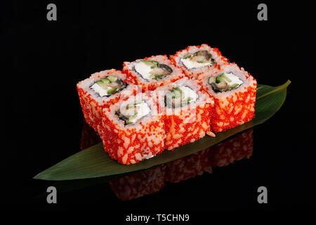 Sushi Walzen aus Reis, geräucherter Aal, Frischkäse und fliegende Fische roe-Tobiko Kaviar auf bananenblatt auf schwarzem Hintergrund Stockfoto
