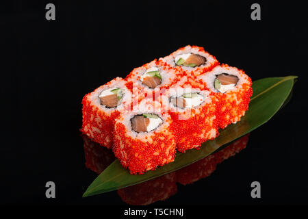 Uramaki philadelphia Rolle mit Lachs, Gurke, Avocado und Rahm Käse gefüllt. Philly Brötchen mit roten fliegende Fische roe auf bananenblatt auf blac Stockfoto