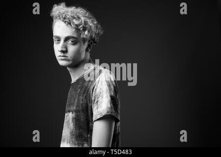 Skinny junger Mann mit lockigem Haar gegen grauen Hintergrund in blac Stockfoto