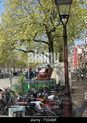 Drei junge Männer sitzen auf einer alten leder Sofa auf einem strassenrand Kabinett unter abgestellte Fahrräder an der Seite des Kanals in Amsterdam verlassen Stockfoto