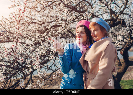 Gerne ältere Mutter und ihrer Tochter umarmen in blühende Frühling Garten bei Sonnenuntergang. Muttertag Konzept. Die Werte der Familie Stockfoto