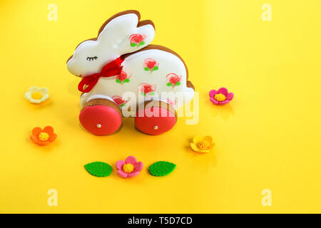 Ostern Konzept, handgefertigte Rosa und weissen Lebkuchen in Form eines Bunny auf gelbem Hintergrund. Lebkuchen Kaninchen, Feder Stockfoto