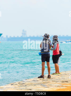 Die Fischer fischen vom Ufer des Hafen von Singapur. Kommerzielle Frachtschiffe im Hintergrund Stockfoto