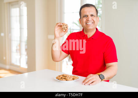 Mittleres Alter Mann essen Chocolate Chips cookies zu Hause mit einem glücklichen Gesicht stehen und lächelnd mit einem selbstbewussten lächeln zähne Stockfoto