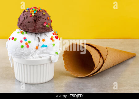 Platte von Vanille und Schokolade Eis schaufeln Schalten besprüht Schokolade Stücke und Waffeln auf gelben Hintergrund. Stockfoto