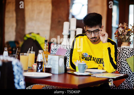 Asiatischer Mann in Brillen und gelbe Sweatshirt sitzt im Cafe und Kaffee trinken. Stockfoto