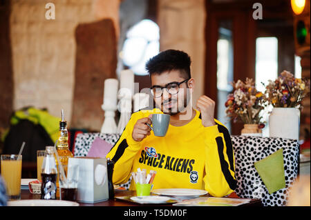 Asiatischer Mann in Brillen und gelbe Sweatshirt sitzt im Cafe und Kaffee trinken. Stockfoto