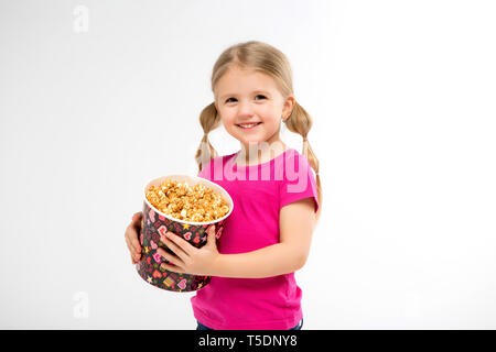 Baby Mädchen mit Popcorn auf weißem Hintergrund isolieren. kleinen niedlichen Baby Mädchen 3-4 Jahre alt mit einem Eimer Popcorn, Kinder Kindheit lifestyle Konzept. Stockfoto