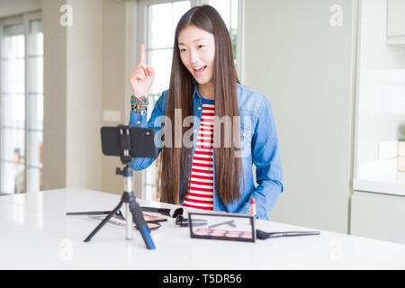 Schöne asiatische Einflussnehmer Frau Aufnahme Make-up Tutorial über Smartphone-kamera Zeigefinger mit erfolgreichen Idee. Verlassen und glücklich. Anzahl Stockfoto