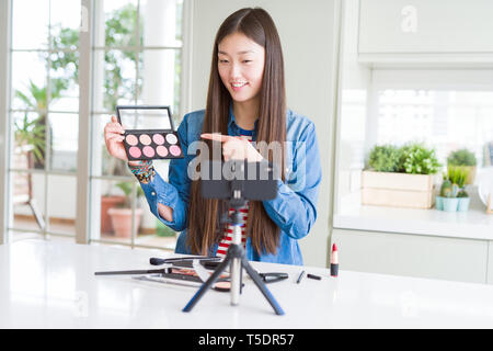 Schöne asiatische Einflussnehmer Frau Aufnahme Make-up Tutorial mit Smartphone Kamera sehr zufrieden zeigte mit Hand und Finger Stockfoto