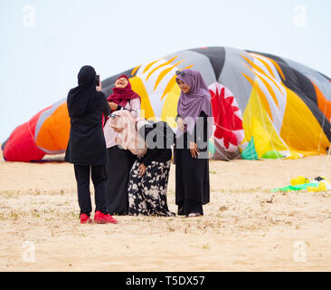 Vier muslimische Frauen tragen Kopftuch Fotografieren am Strand in der konservativen Kelantan Zustand von Malaysia. Im Hintergrund ist eine große deflationiert Kite. Stockfoto