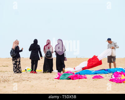 Vier muslimische Frauen tragen Kopftuch zu Fuß am Strand in der konservativen Kelantan Zustand von Malaysia. Neben ihnen ein Mann seine deflationiert weichen Ki vorbereiten Stockfoto